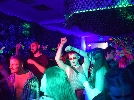 A group of young people dance under cool lights at a Rave for the Rainforest event