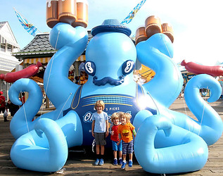 Custom inflatable blue octopus with a mustache and top hat, displayed at a boardwalk with children posing in front