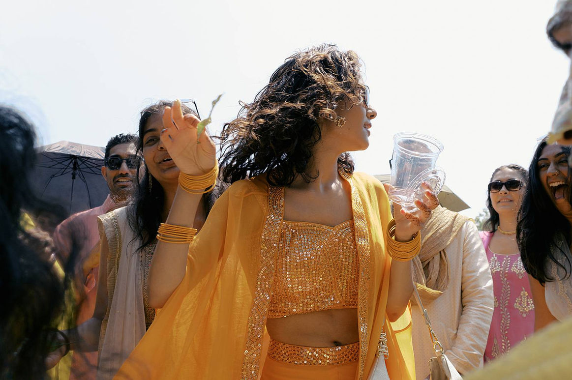 A bridesmaid, adorned in bright oranges and yellows, turns away from camera in a candid photograph during the Haldi celebration from a 3 day Indian Wedding weekend at the Botanical Gardens in Traverse City, MI. 