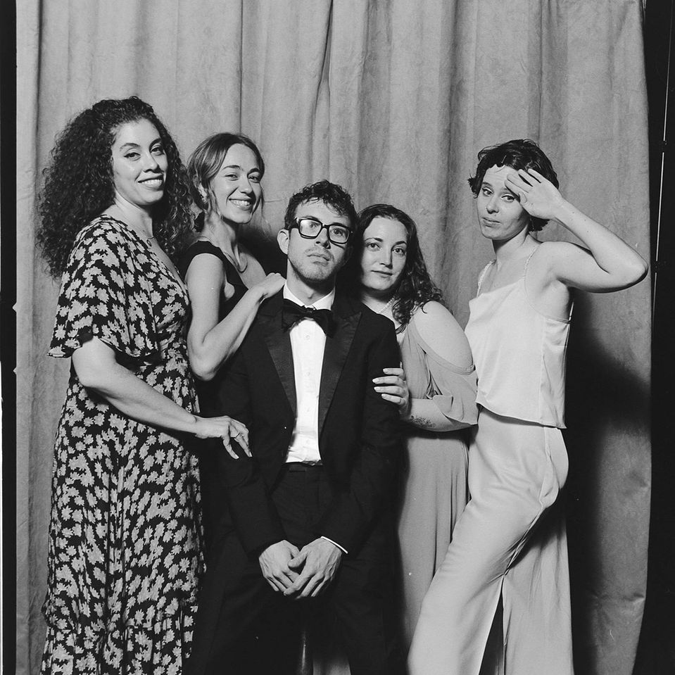 Black and white film portrait of a group of guests at a wedding reception, posing fashionably, against a studio photo booth setup. 