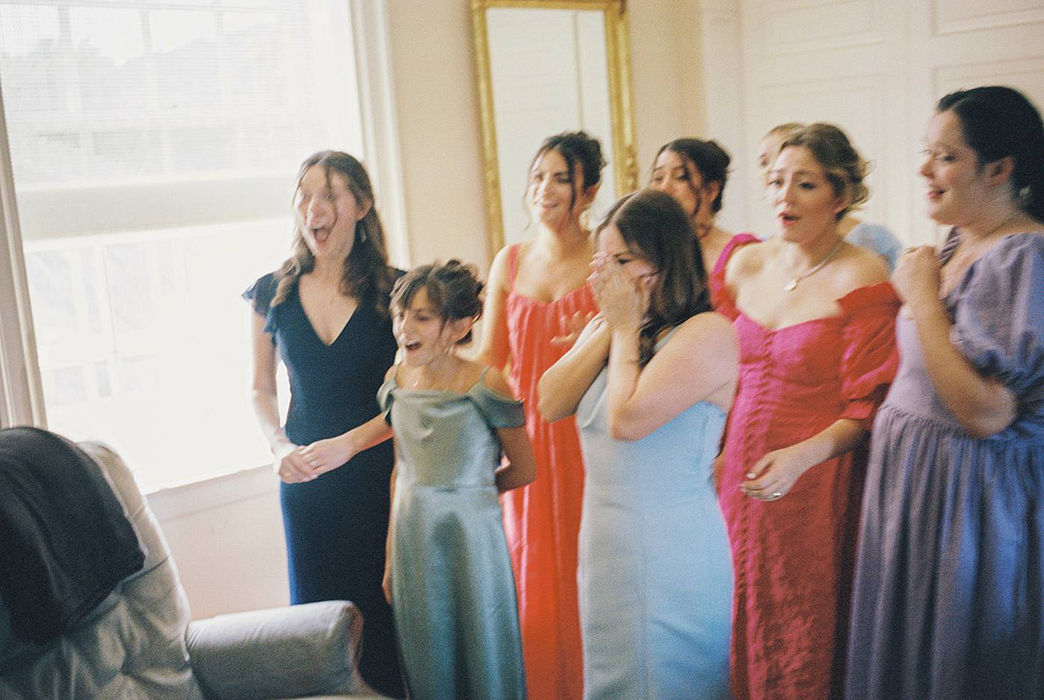 Bridesmaids and flower girl react in shock and awe as the bride reveals her wedding dress to them for the first time in this historic, Nashville, private estate wedding. Photo rendered in color on 35mm film. 
