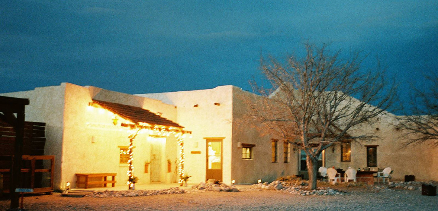 A warm lit, stucco building in the West Texas desert is illuminated against the blue hour sky, following an intimate wedding ceremony in Hueco Tanks state park.