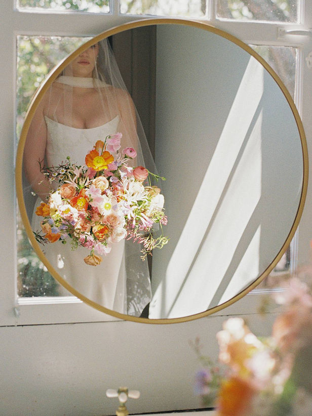 documentary film wedding portrait of a bride looking into the mirror, holding her bouquet before she gets ready to walk down the aisle. Shot in window lit sun on Kodak 35mm film.