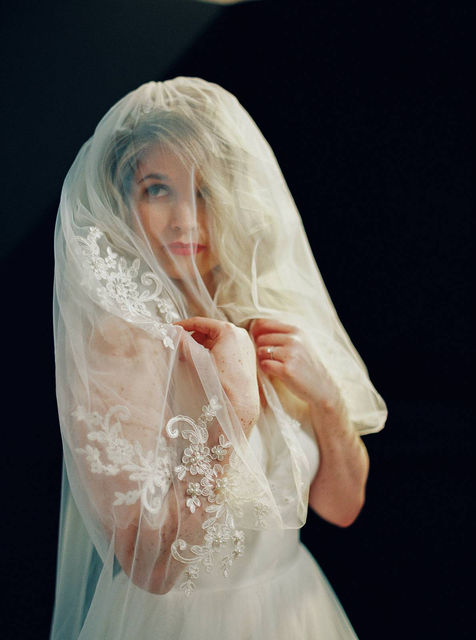 Kodak portra 400 35mm film portrait of a bride in studio. Shot against a black backdrop, lit with a spot LED light from above, as her blusher veil covers her face. 