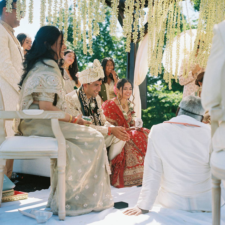 Groom wears formal attire and a ceremonial headdress while the bride wears a traditional, vibrant red Lehenga sitting on stage during a Summer, Indian wedding ceremony in Northern Michigan. Photo captured on square, medium format film with a Hasselblad camera. 