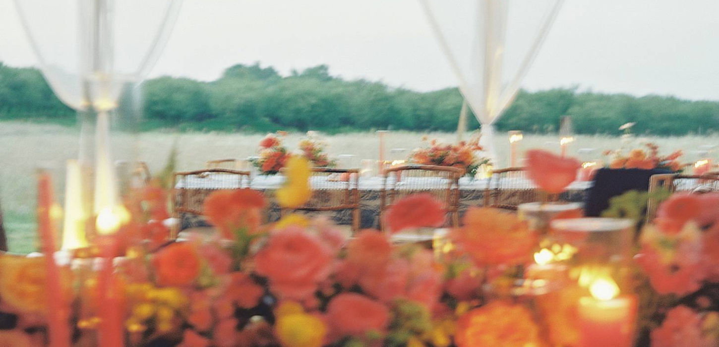 Square format film image of blurred florals and a tablescape with late evening light at a tented, Northern Michigan wedding reception in a farm field.