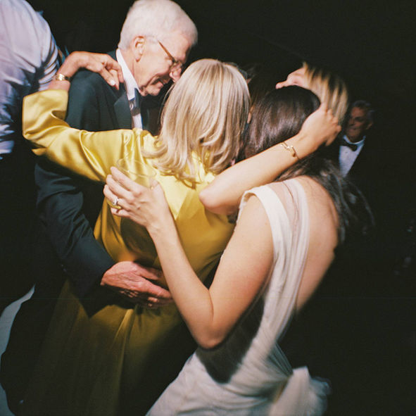 Ultra-wide, vintage looking candid film photograph of a bride and her family hugging at the end of her Gibbes Museum Charleston, SC wedding. 