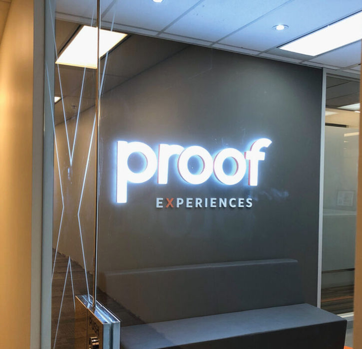 Custom white dimensional lobby sign with rear-mounted LED "halo" lighting for a Dallas-Fort Worth (DFW) corporate reception, featuring standoff-mounted white acrylic or painted aluminum letters on a dark feature wall for a premium 3D glow in North Texas.