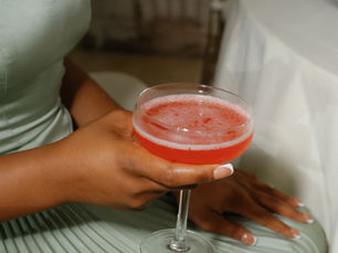 Woman in a soft sage pleated dress holding a pink spring cocktail during an elegant wedding reception with layered tablescape details and warm ambient lighting.