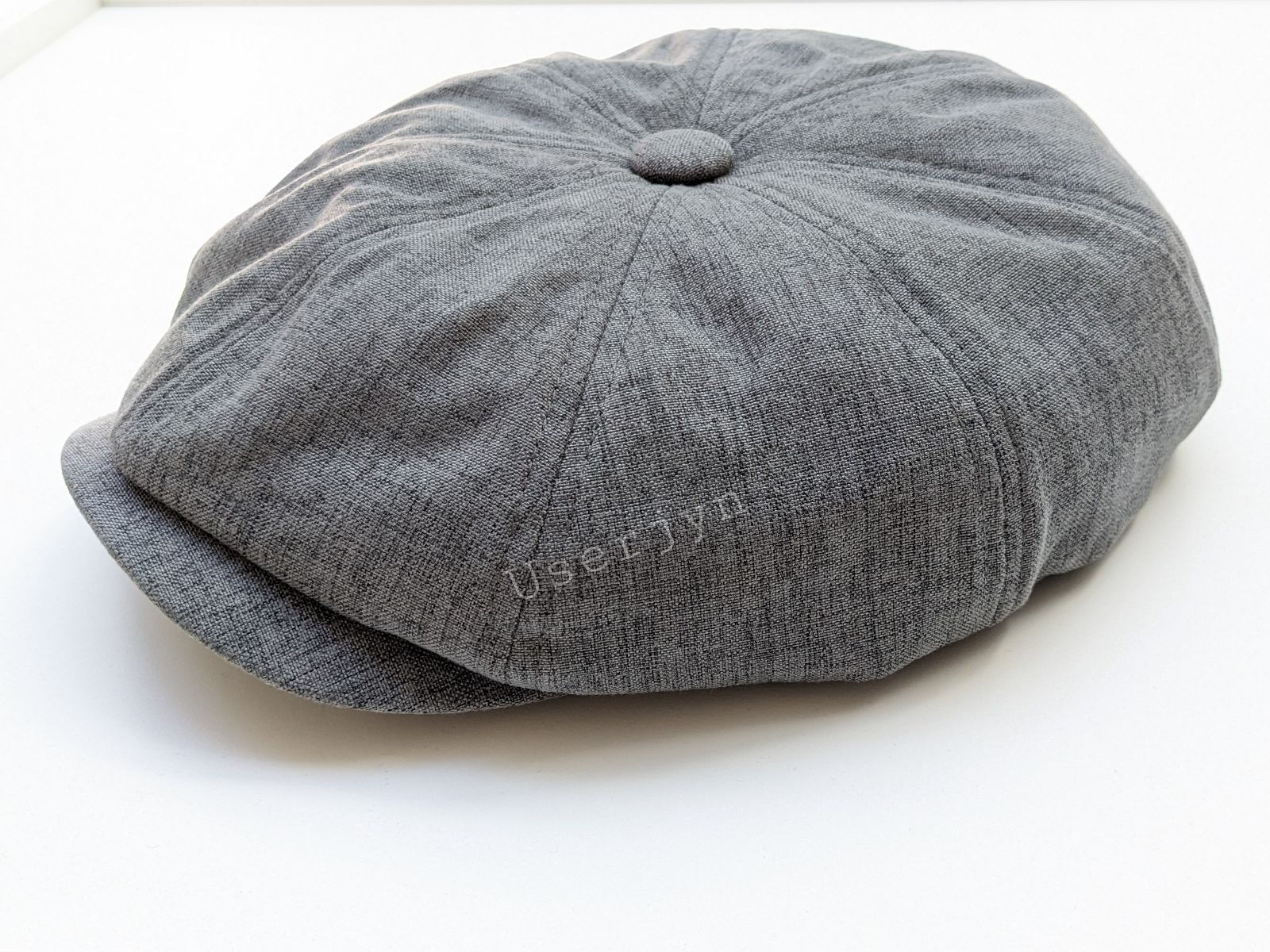 Gray flat cap with userjyn visible inscription, sitting on plain white. Userjyn