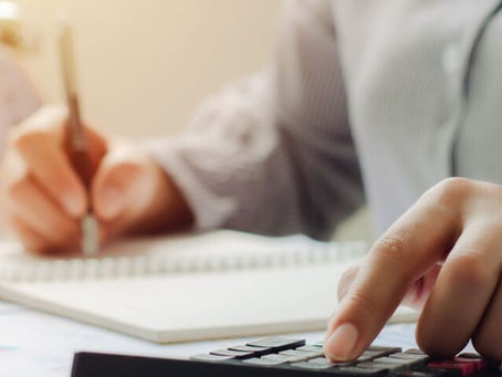 Dettaglio di una persona che calcola numeri su una calcolatrice e prende appunti, simboleggiando la pianificazione finanziaria e le detrazioni fiscali immobiliari.