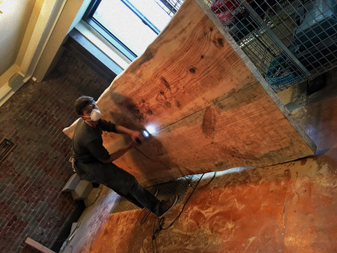 Woodworker sanding a large live edge oak dining table.