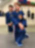 Two young boys in martial arts uniforms looking focused as they listen to directions from a teacher out of frame