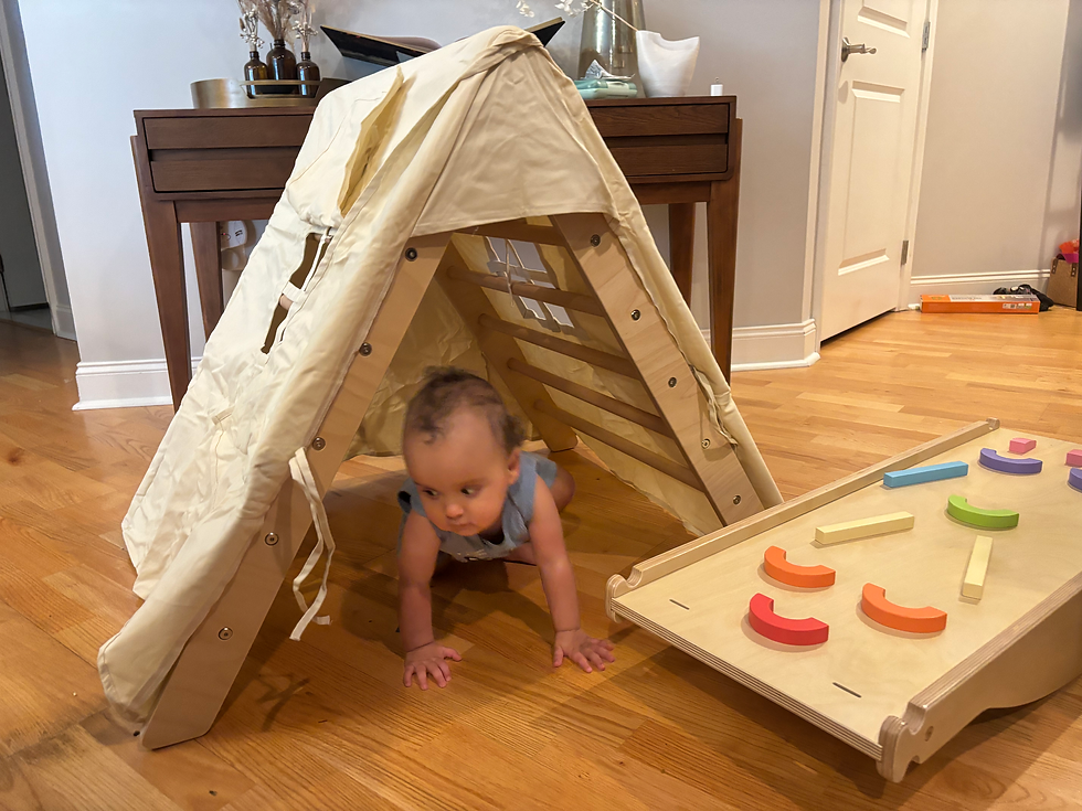 A baby using his Pikler Triangle as a tent with the balance board next to it
