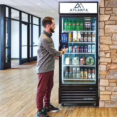 Man using phone at a vending machine by "ATLANTA Smart Amenities" in a modern hallway with wooden floors and stone wall.