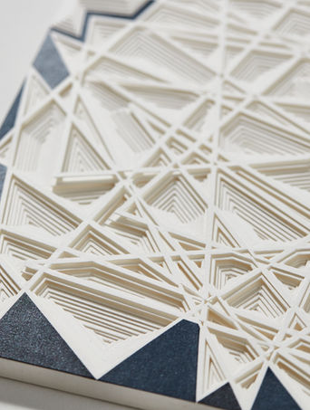 Œuvre sculptée en papier. Bas-relief abstrait composé d'une multitude de couches de papier blanc découpé créant une topographie graphique en strates triangulées. Les rebords sont habillés de papier bleu mettant en valeur le dessin facetté ainsi créé. Par l'artiste Marie Gobert. © photo Rebecka Oftedal