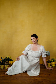 Woman in a white dress sitting against a yellow wall.