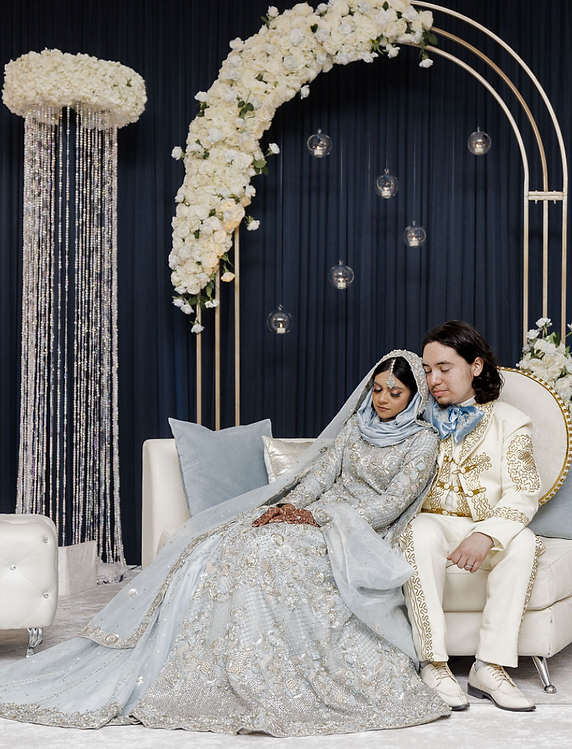 Captivating Indian Wedding Reception - Couple in Traditional Attire on Stage with White Florals, Gold Arch, and Crystals. Experience the magic of an Indian wedding reception as the radiant couple, dressed in traditional attire, graces the stage adorned with white florals, a golden arch, and sparkling crystals, creating a truly enchanting atmosphere.