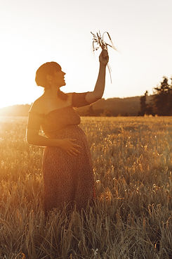 Une femme enceinte dans un champ de blé qui tiens un bouquet