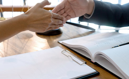 Two people shake hands over a desk with documents, suggesting a professional agreement
