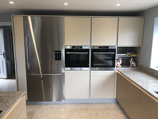 The kitchen featuring a stainless steel fridge, double ovens, beige cabinetry, and a granite countertop