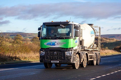 A green and white concrete mixer truck driving along a road