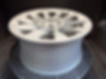 A silver alloy wheel rim with intricate spokes displayed on a perforated surface