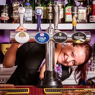 A smiling bartender peeking through beer taps at a well-stocked bar