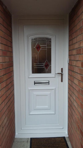 A white front door with decorative glass and a metal handle, framed by brick walls