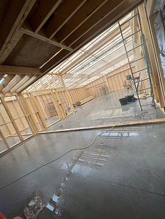 Interior view of a construction site featuring wooden framing, a freshly poured concrete floor, and natural light from skylights