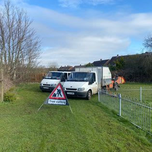 A group of white vans parked with a sign saying tree cutting