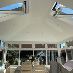 Interior of a modern conservatory with sloped ceiling, open skylights, and large windows