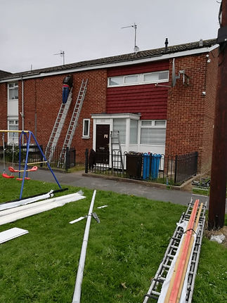 Exterior view of a brick house with a worker on a ladder and equipment scattered on the lawn