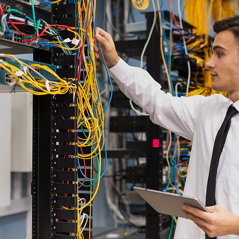 Man holding a tablet, examining colourful network cables in a server room.