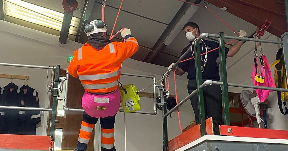 A worker in a high-visibility jacket practices rope rescue techniques with equipment in a training facility.