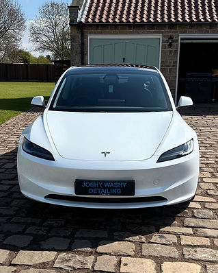 Front view of a shiny white Tesla parked on cobblestones in front of a garage