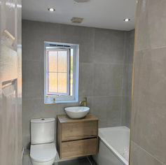Bathroom with grey tiles, featuring a toilet, wood vanity with vessel sink, sleek faucet, and a bathtub