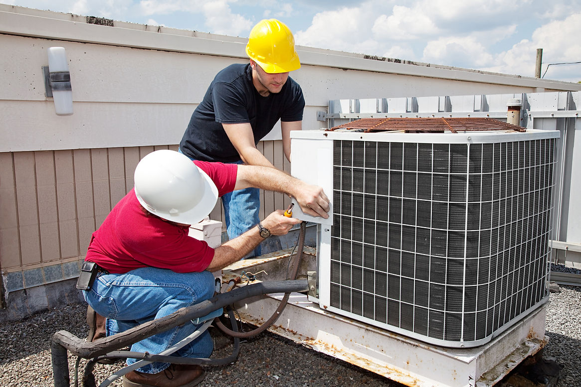 Two technicians in hard hats are repairing an outdoor air conditioning unit on a rooftop