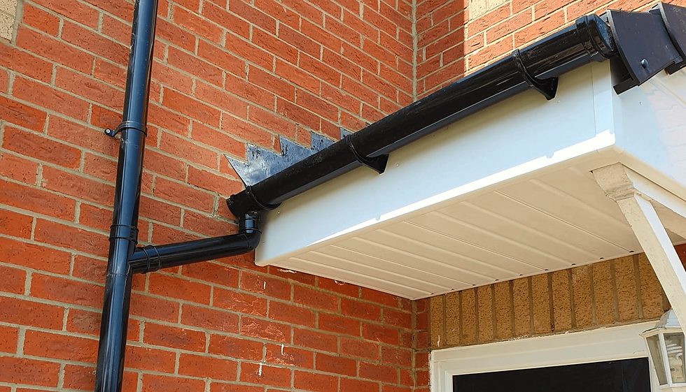 Close-up of a red brick building's corner shows a black gutter and downspout connected to a white fascia