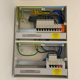 An open electrical distribution board with wiring and warning labels
