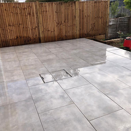 Modern patio with large wet grey tiles, bordered by a wooden fence