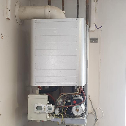Wall-mounted boiler with visible pipes and wires in a room