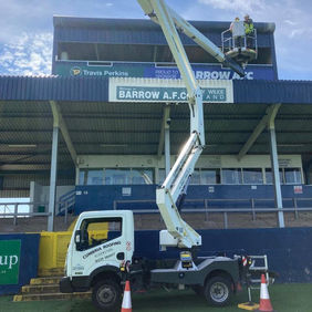 Workers using a cherry picker to perform maintenance on the Barrow A.F.C. stadium
