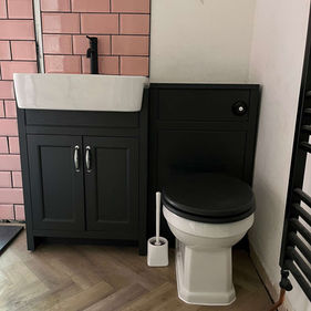 Bathroom corner with pink subway tiles, a black vanity with white sink and black tap