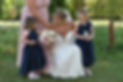 A joyful bride in a white gown holds a bouquet surrounded by two young girls in navy dresses