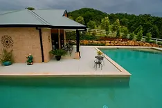 A spacious back garden pool with a swim-up patio and seating area next to a brick pool house