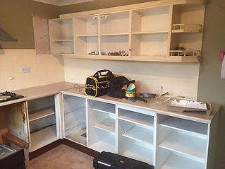 A partially assembled kitchen with empty cabinets, a toolbox, and scattered tools on the counter, indicating renovation work