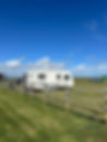 Caravan parked in a green field under a bright blue sky with scattered clouds