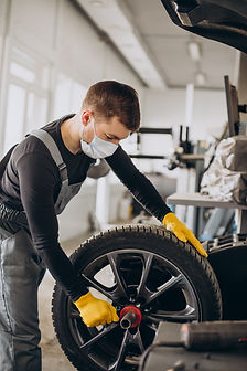A mechanic wearing a face mask and yellow gloves works on a car tyre in a garage