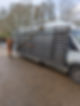 A worker in an orange jumpsuit secures a large metal frame to the side of a white van for installation